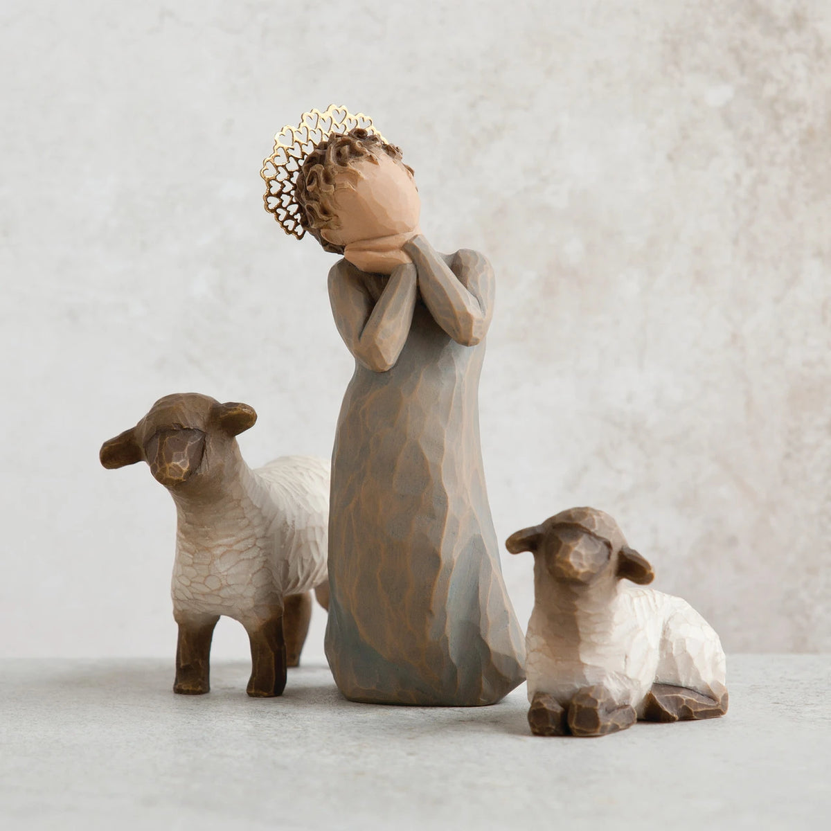 Close view of small angel figurine in dark tan dress holding hands up to face, in between to white/brown lamb figurines
