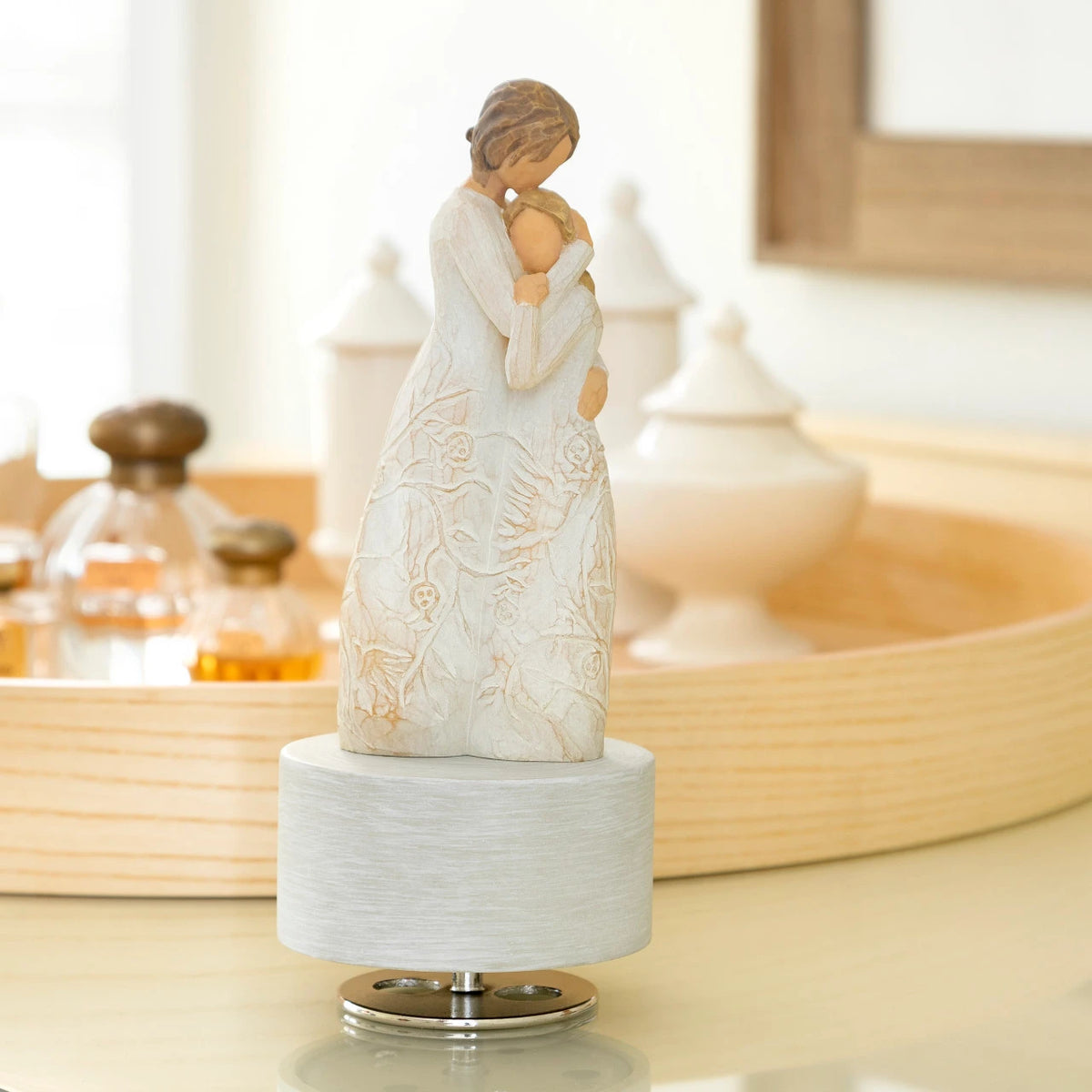 Willow Tree Close to Me Musical, 7.5”h hand-painted resin figure of woman embracing tween girl, both in cream dresses carved with intertwined vines and leaves, atop round, cream base containing musical element, on dressing table