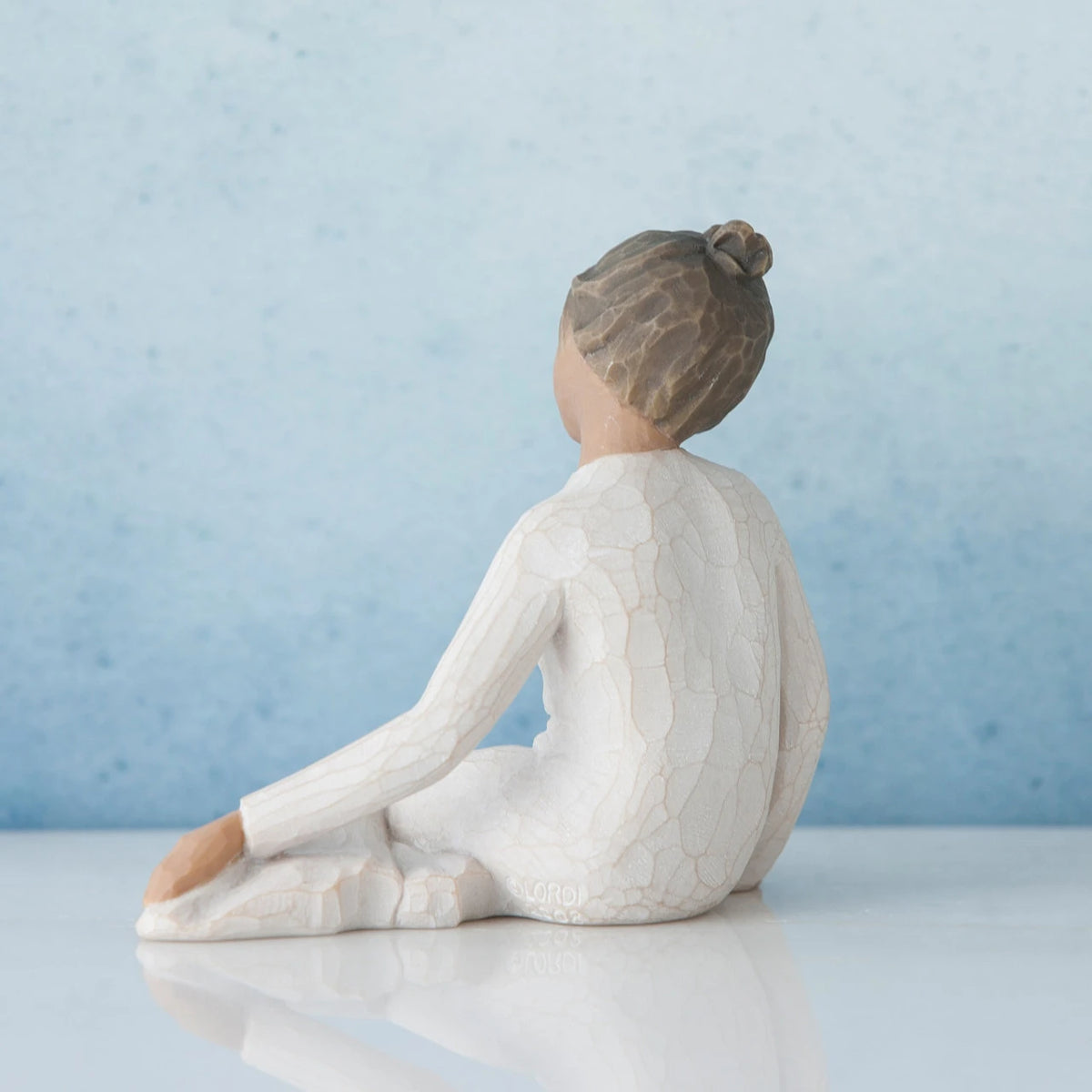 Small brunette girl figurine in white dress sitting away from the camera - blue background
