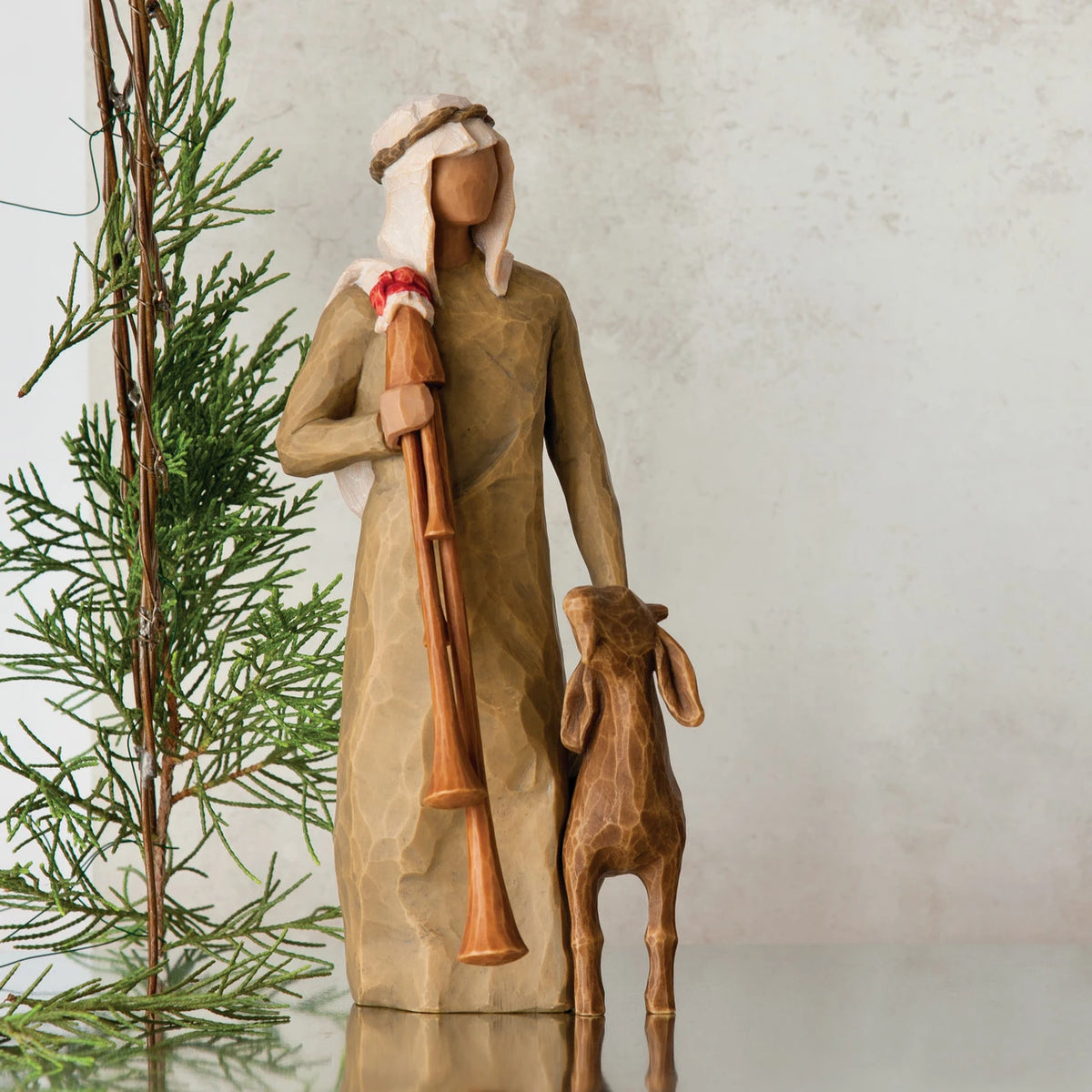 Wiseman figurine in tan dress next to golden lamb figurine with green tree in the background