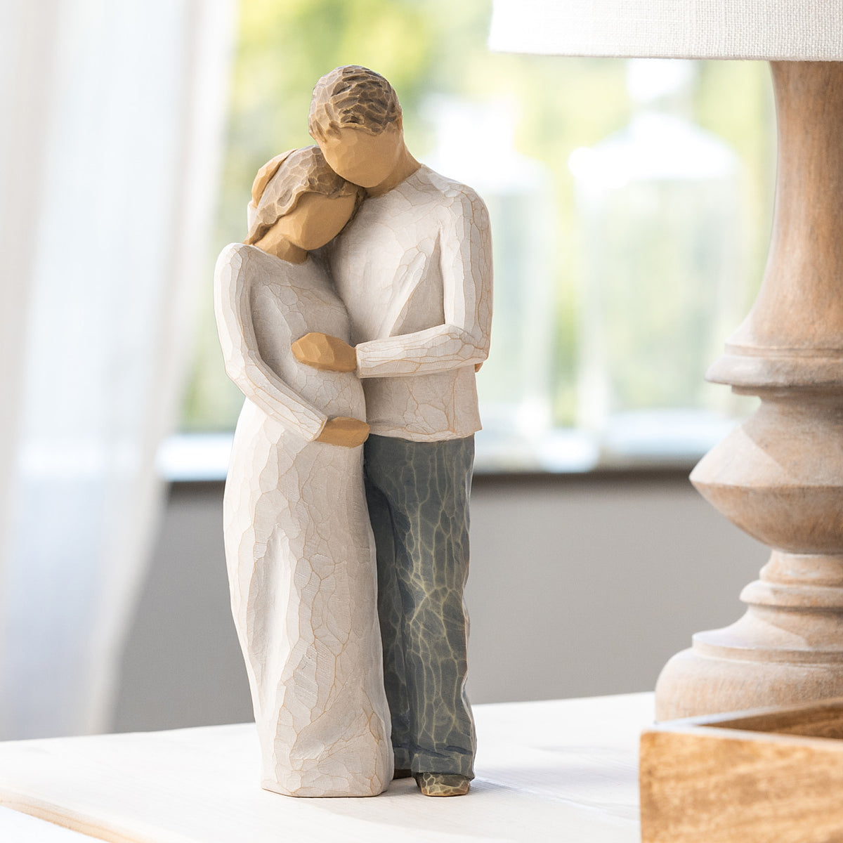 Willow Tree Home, 8.5”h hand-painted standing figure of man and pregnant woman embracing, both in neutral clothes, on table near window