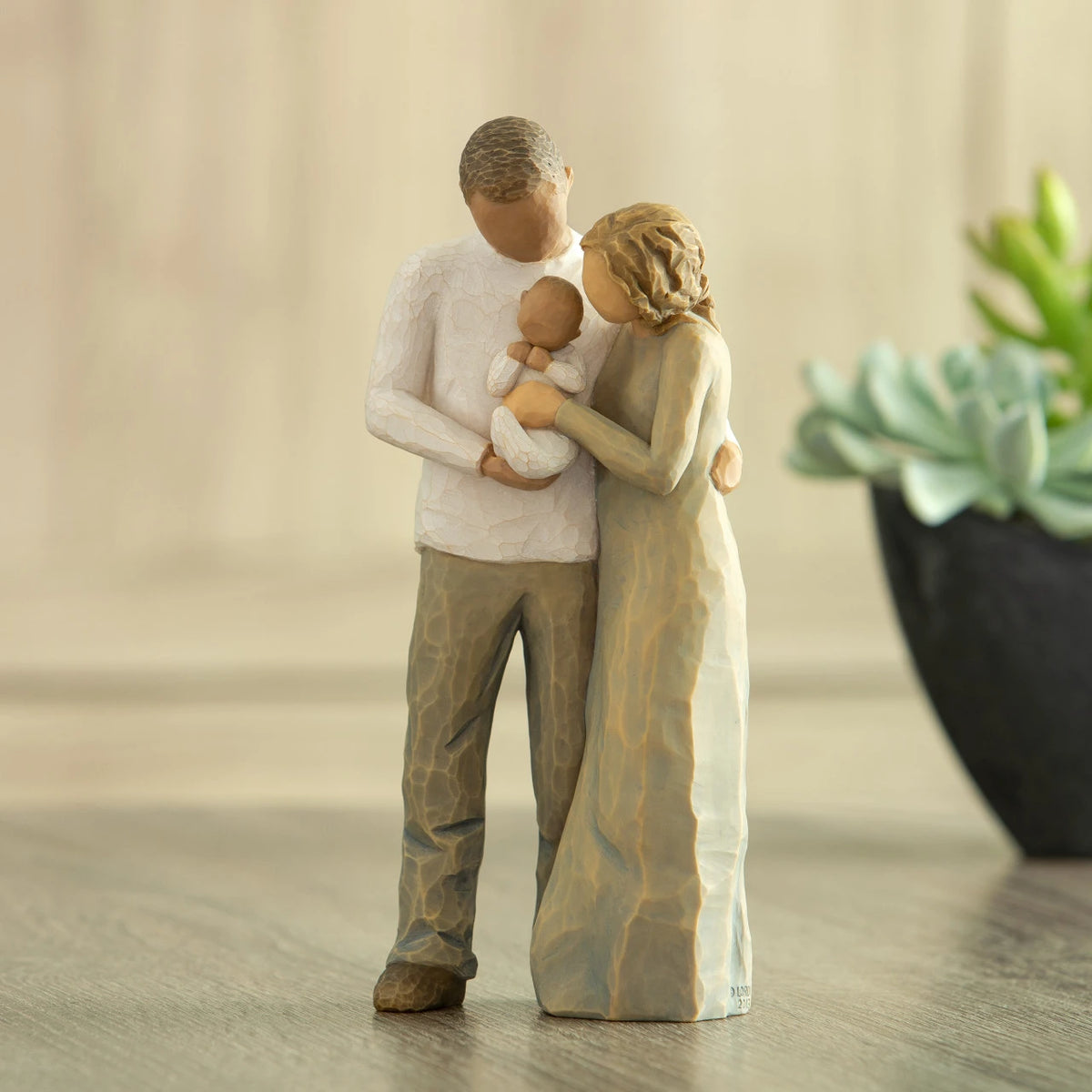 Front view of standing couple, woman has lighter skin and hair; man has darker skin and hair, holding a baby between them. Potted succulent in background.