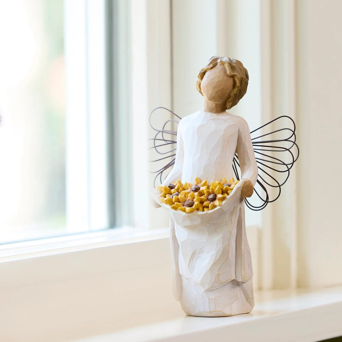 Willow Tree Sunshine, 5.5”h hand-painted standing resin angel with darker skin and hair, cream dress and wire wings, holding up skirt full of Black-Eyed Susans, on windowsill