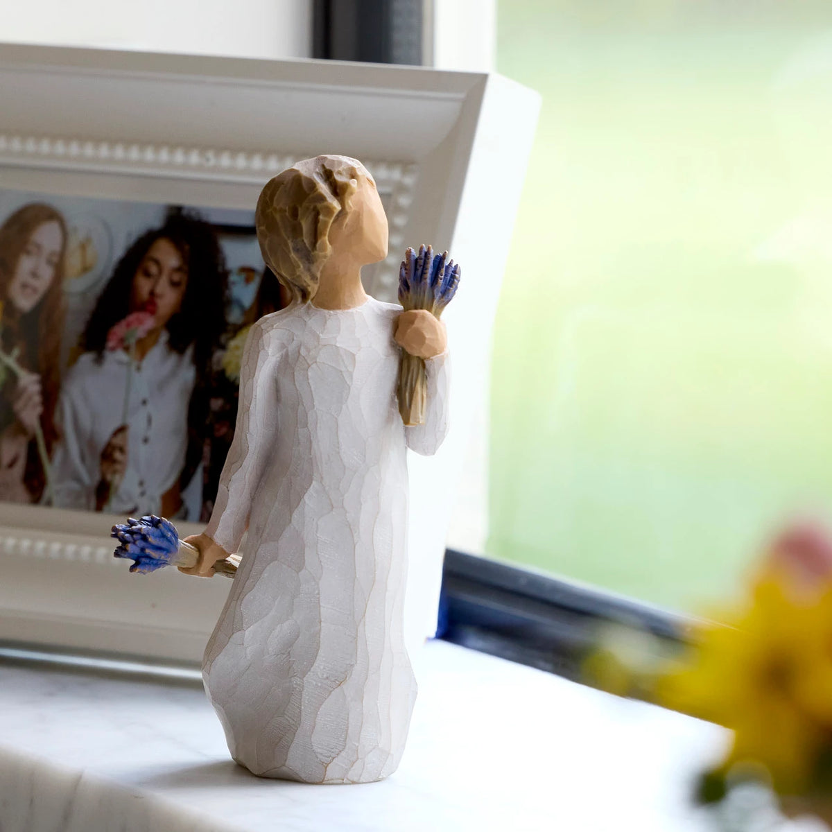 Willow Tree Lavender Grace, 5.5”h hand-painted standing resin figure in cream dress, holding two bundles of lavender flowers - one in raised hand, one at her side, on windowsill