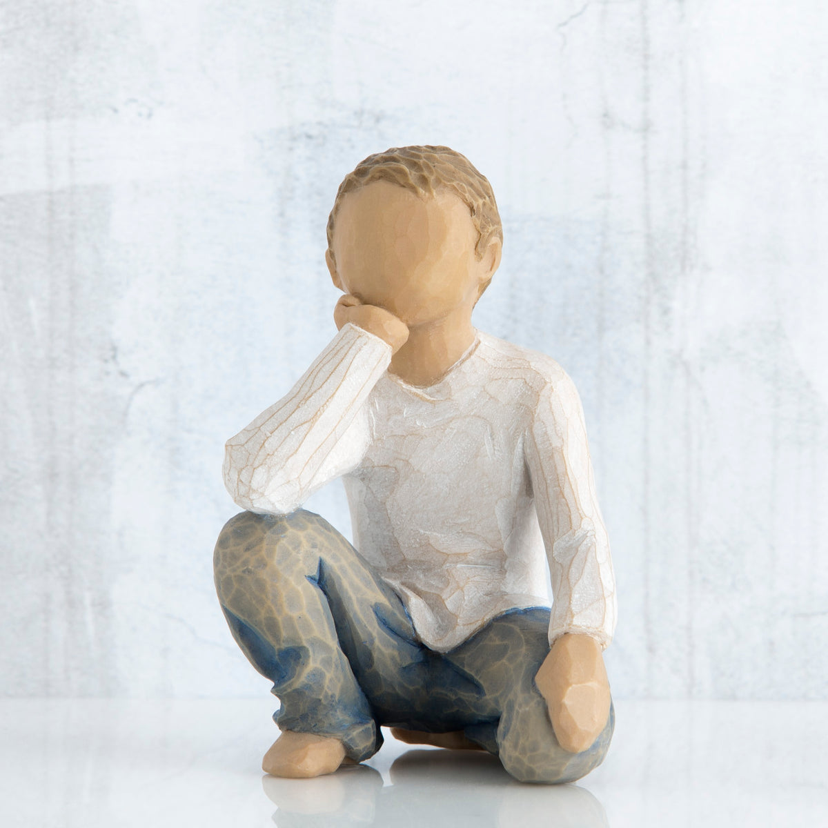 Small faceless boy figurine sitting with elbow on knee - wearing white shirt and blue jeans