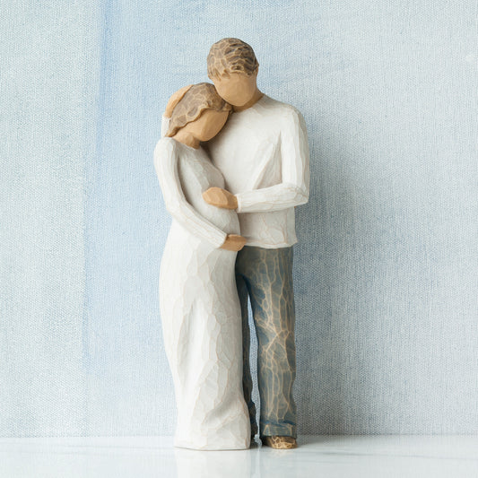 Willow Tree Home, 8.5”h hand-painted standing figure of man and pregnant woman embracing, both in neutral clothes, in front of grey blue painting