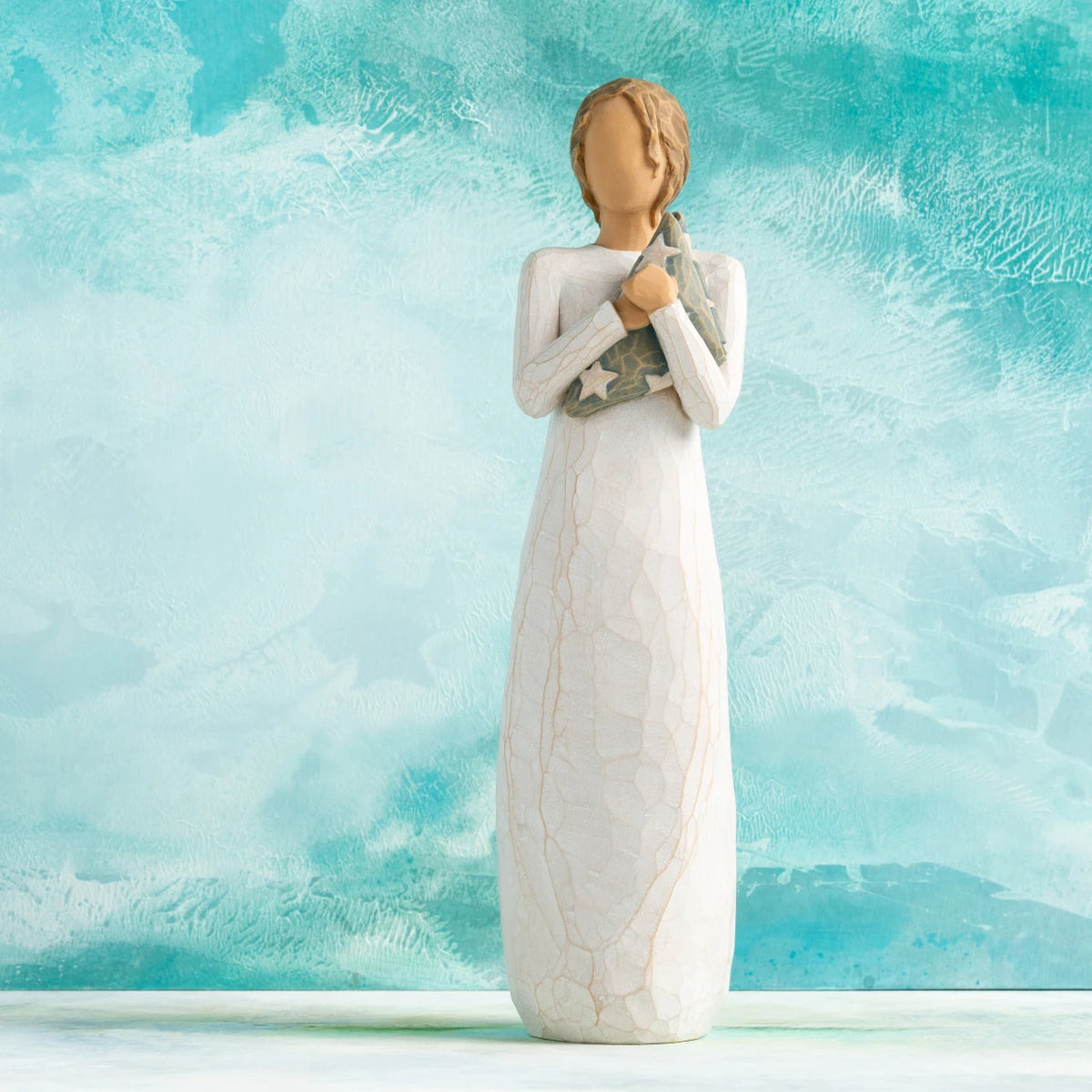 Willow Tree Hero, 9.5”h hand-painted standing resin figure in cream dress holding folded American flag in her arms,  in front of aqua painting