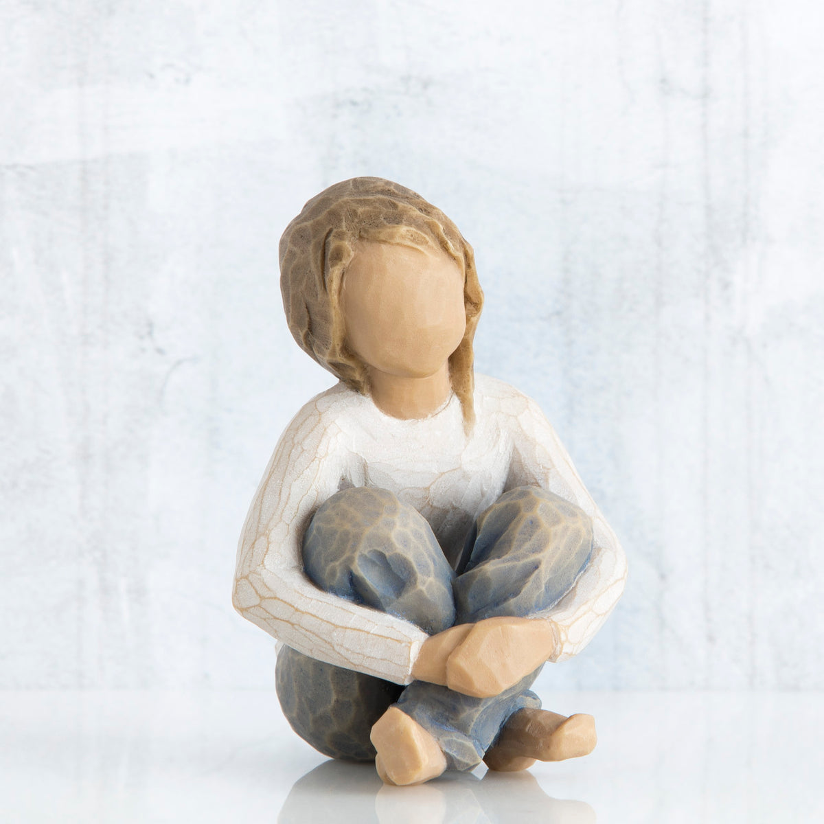 Little girl figurine sitting with legs crossed - faceless - wearing white shirt and blue jeans