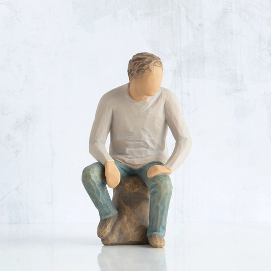Front view, adult male figure in light gray shirt and blue jeans, seated on gray rock