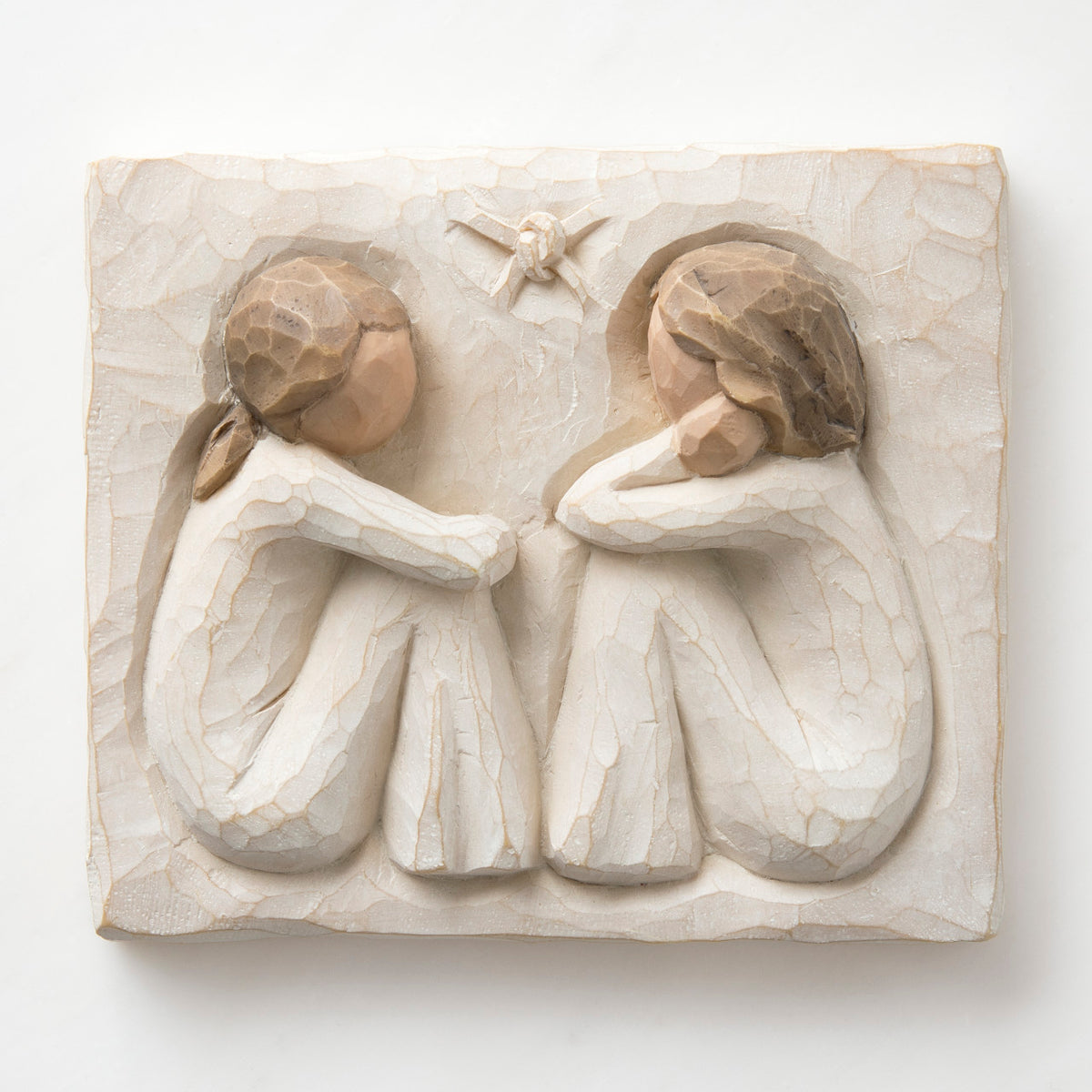 Close up white square carving - two faceless girls sitting looking at eachother wearing white dresses