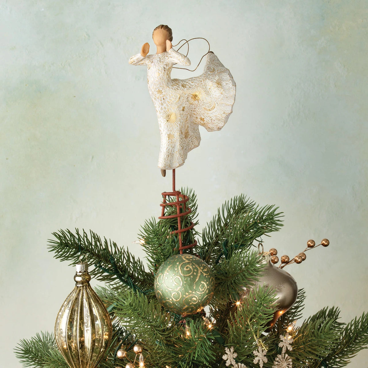Angel figurine in white dress standing on stand on green tree branches and ornaments