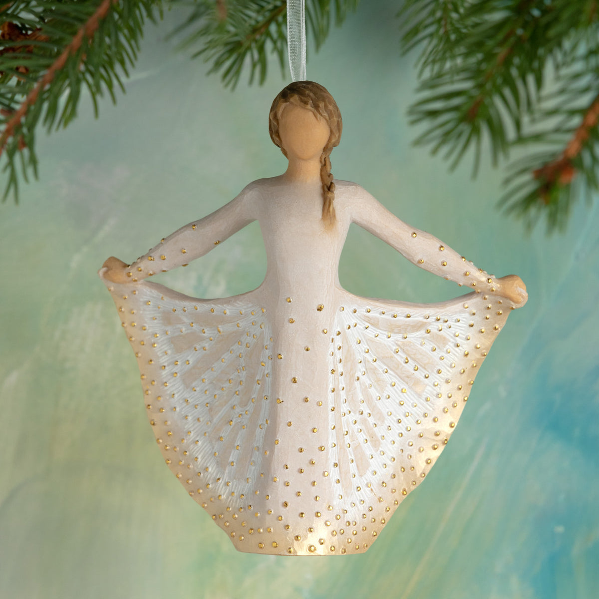 Willow Tree Butterfly Ornament, 4.75”h hand-painted resin figure in cream dress, holding sides of skirt out with hands, skirt has carved markings of a monarch butterfly with gold leaf, sparkly white ribbon, hanging in front of deep teal painting