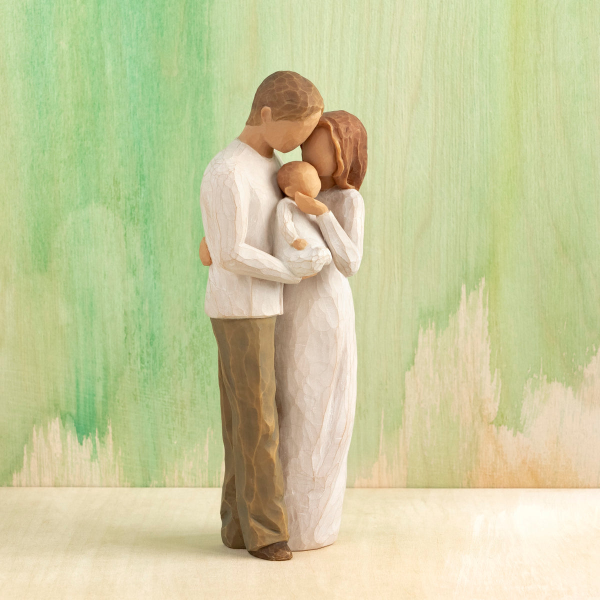 Willow Tree Our Gift, 8.5”h hand-painted resin figure of standing couple holding baby between them, all in neutral clothing, in front of green painting