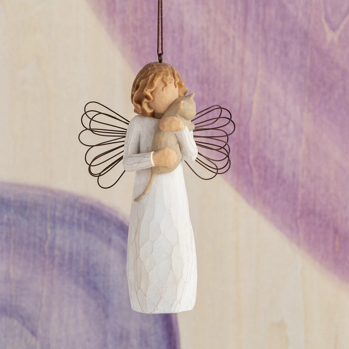 Willow Tree With affection Ornament, 4.5”h hand-painted resin figure in cream dress with wire wings, holding gray cat, brown elastic cord, hanging in front of purple painting