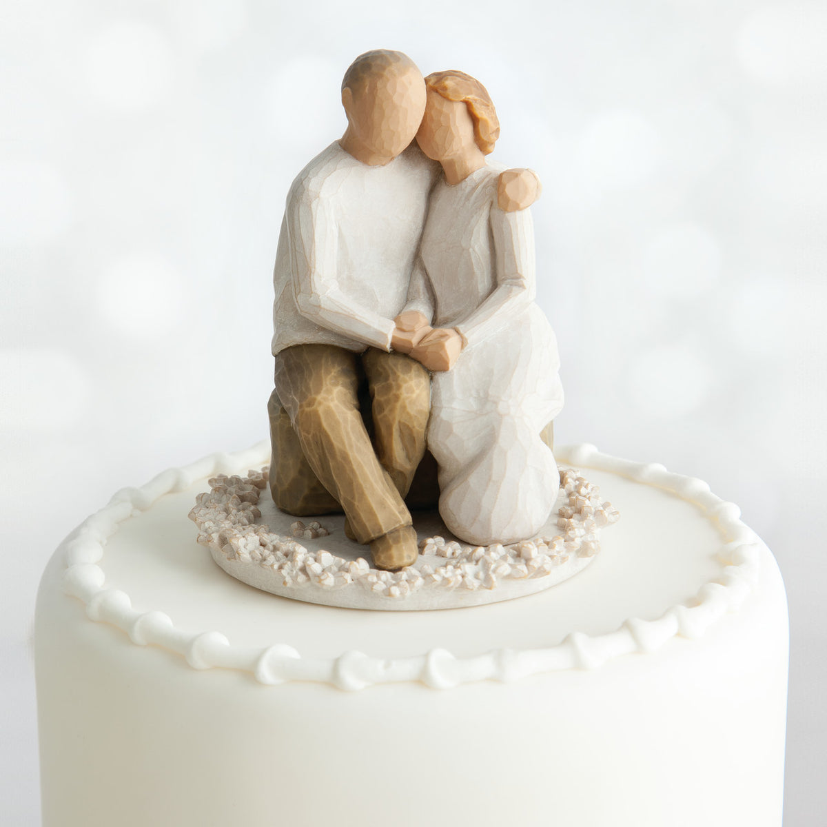 Willow Tree Anniversary Cake Topper, 4”h hand-painted resin figure of seated older couple on bench, holding hands, both in neutral colors, affixed to 3.5" diameter food-safe base of carved white flowers