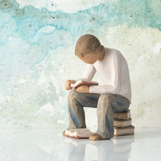 Willow Tree Quest, 4”h hand-painted resin figure of young man in neutral clothes, seated on stack of books and reading, in front of green painting