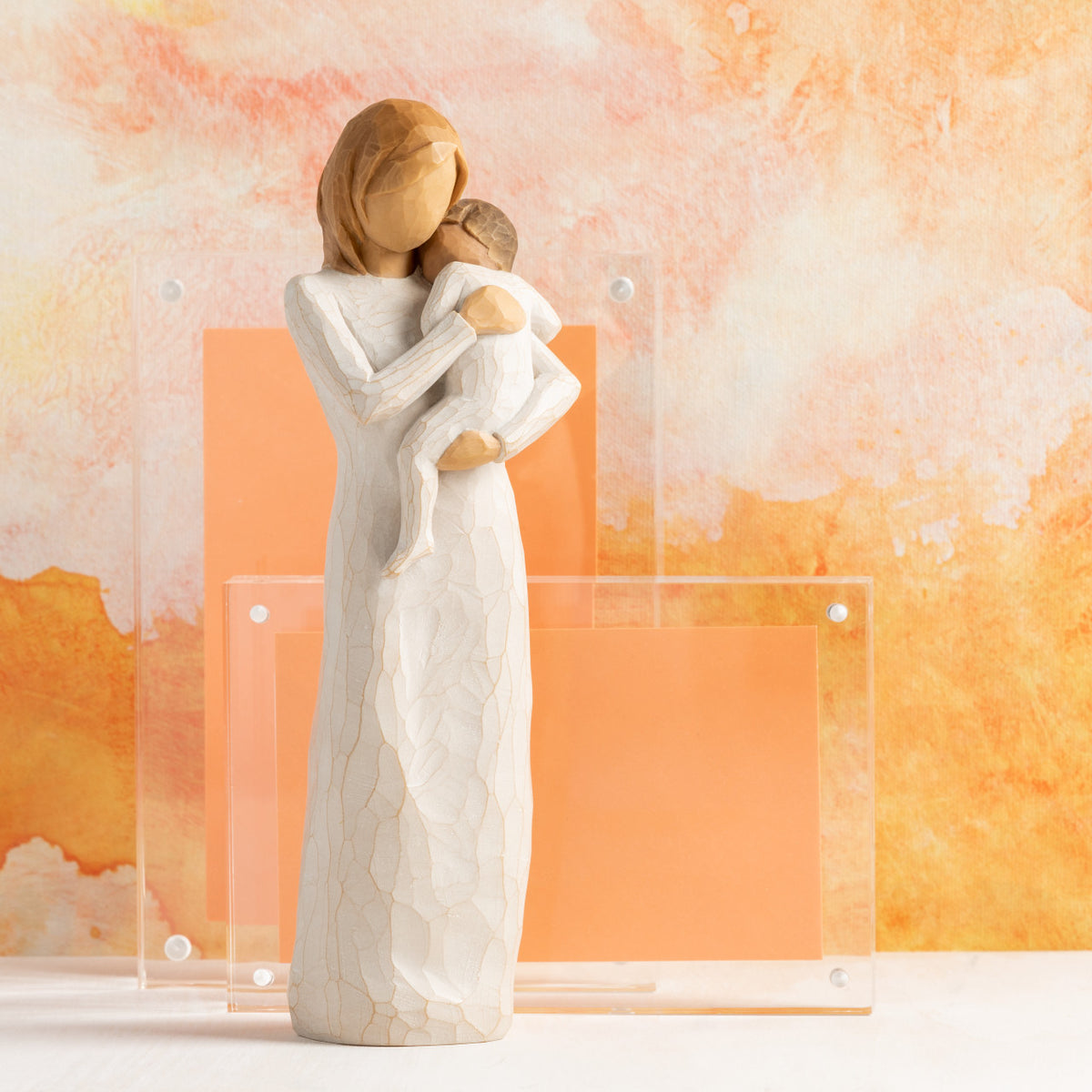 Willow Tree Child of my Heart, 9”h hand-painted standing resin figure holding toddler, both in cream clothes, in front of orange painting