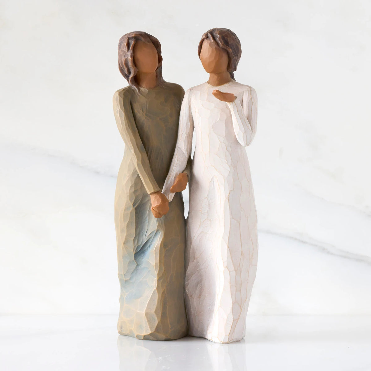 Front view: Figure of two women with darker skin tones in different colored dresses, standing arm in arm