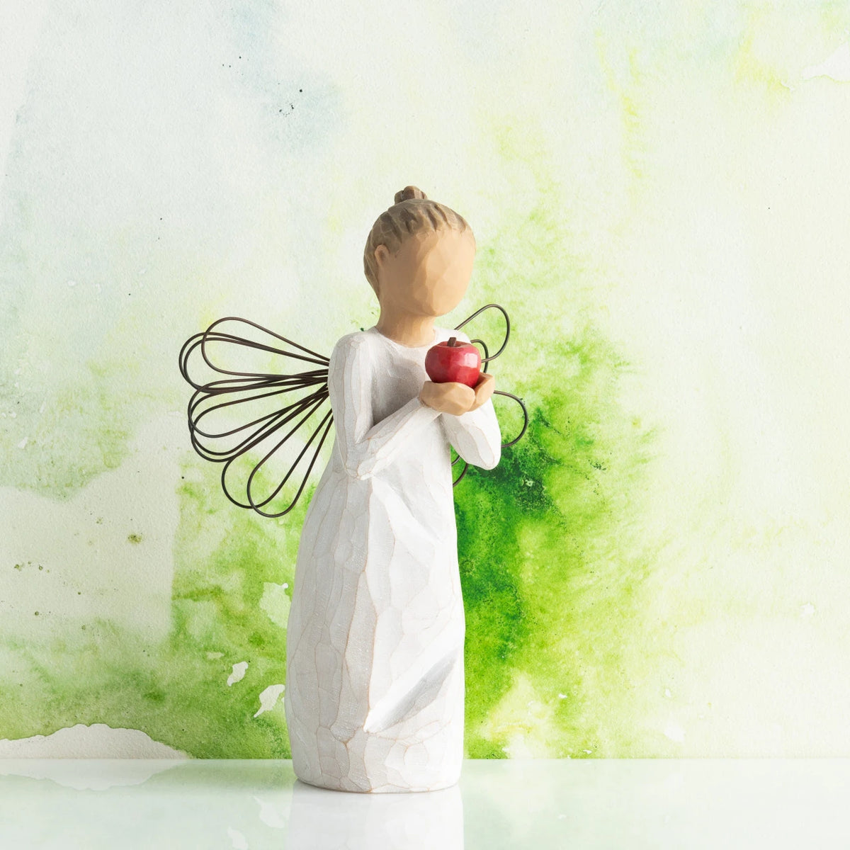 Willow Tree You're The Best!, 5.5”h hand-painted standing resin angel figure in cream dress with wire wings, holding red apple in outstretched hands, in front of green painting