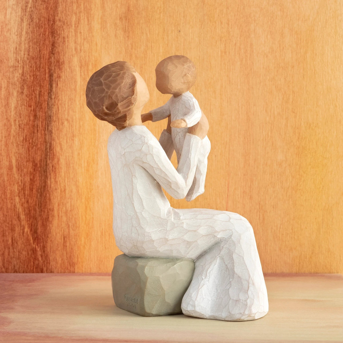 Willow Tree Grandmother, 5.5”h hand-painted resin figure of seated older woman in cream dress, holding baby up in the air, in front of orange painting