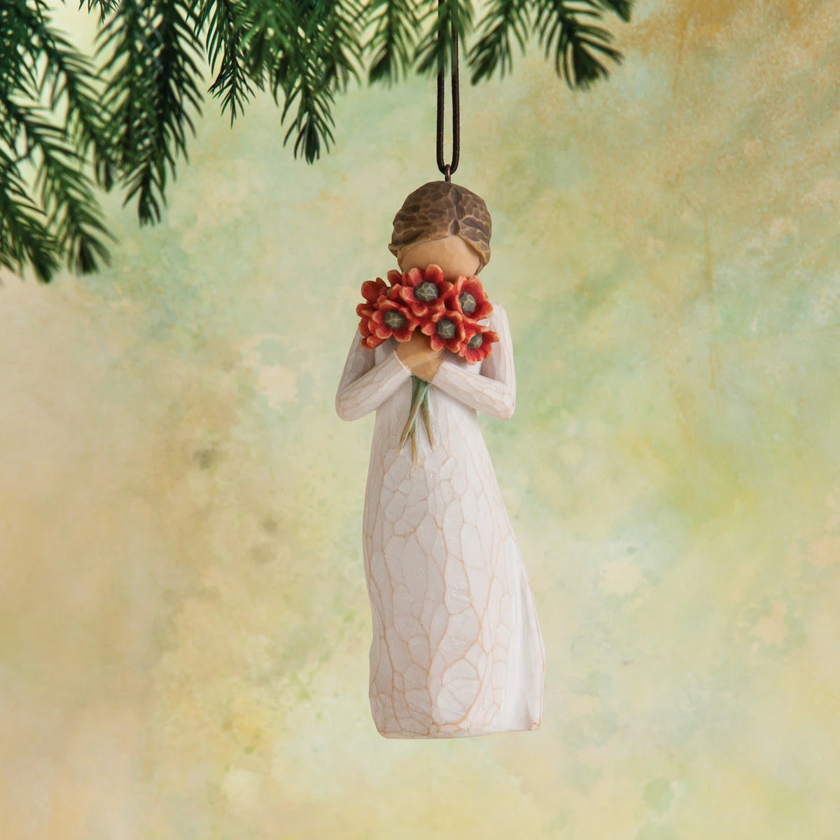 Willow Tree Surrounded by Love Ornament, 4”h hand-painted resin figure in cream dress holding bouquet of poppies to face, brown elastic cord, hanging in front of dark yellow painting