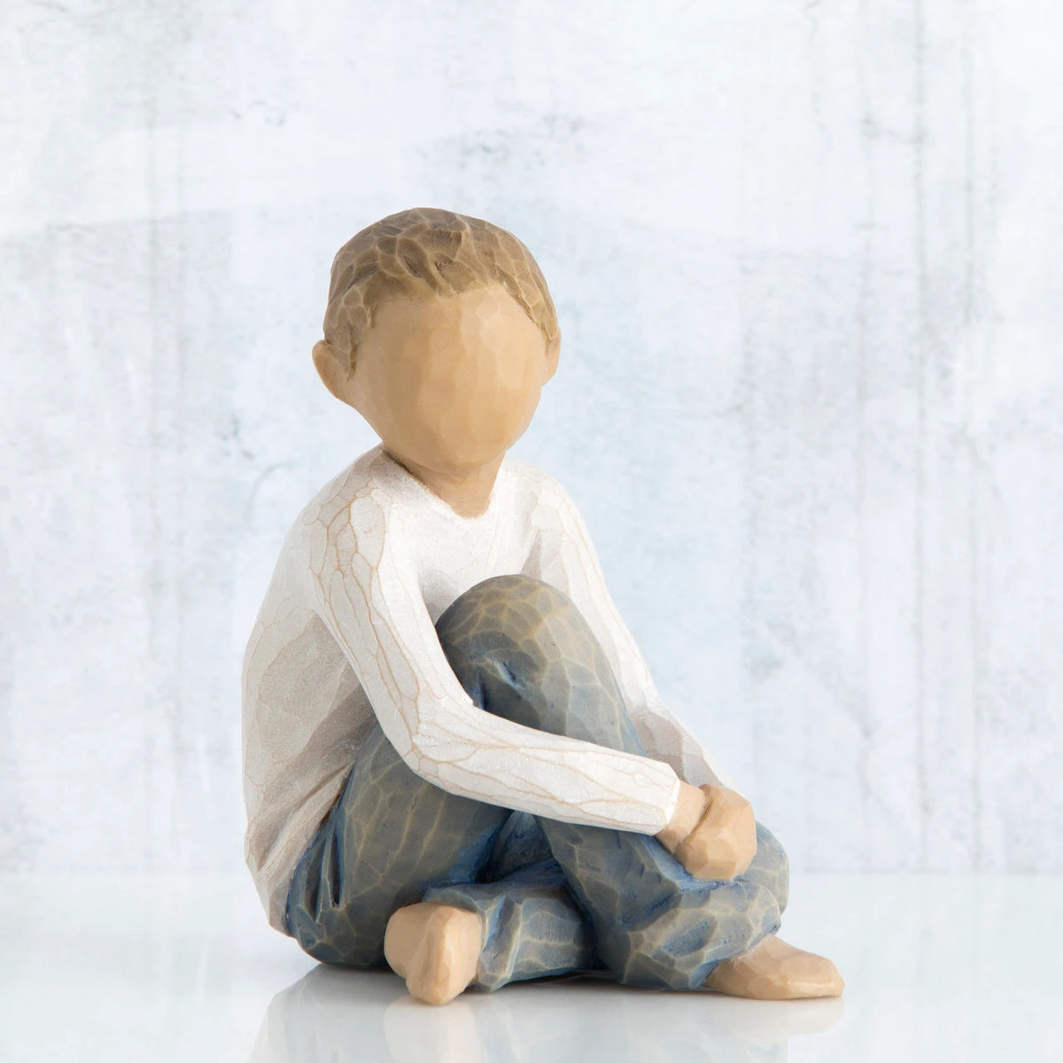 Little boy figurine sitting with hands over knees - faceless - wearing white shirt and blue jeans