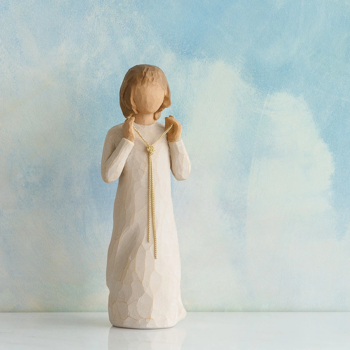Willow Tree Truly Golden, 5"h hand-painted standing resin figure in cream dress, holding a knotted, long gold chain between her hands, in front of dusty blue painting
