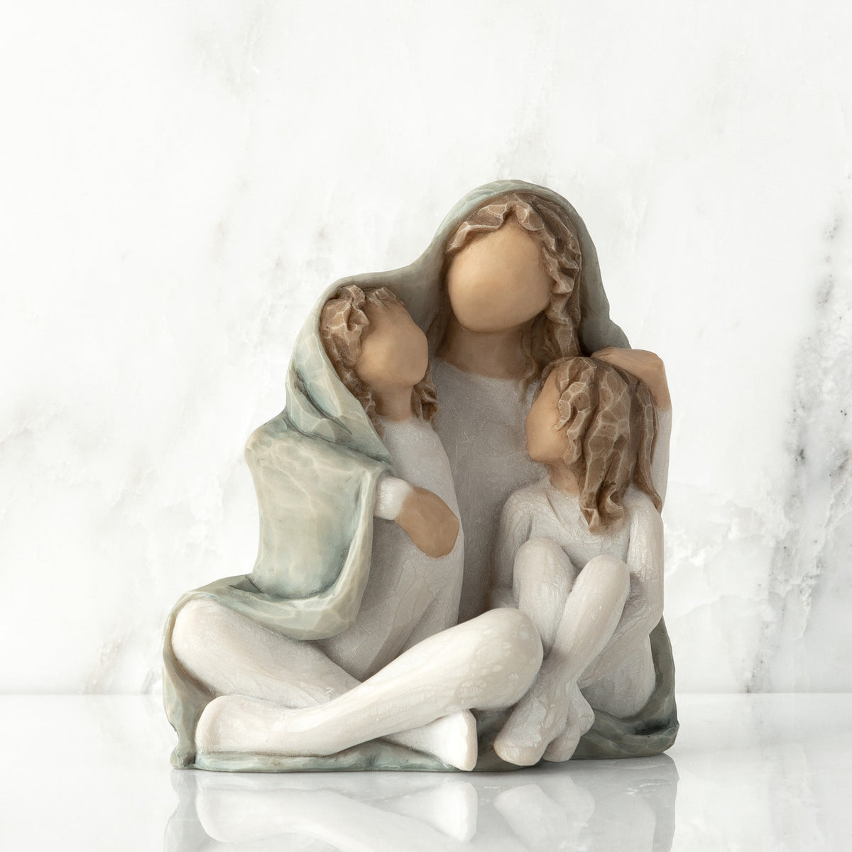 Front View: seated figure with arms around two younger figures, all wrapped in a blue-gray blanket