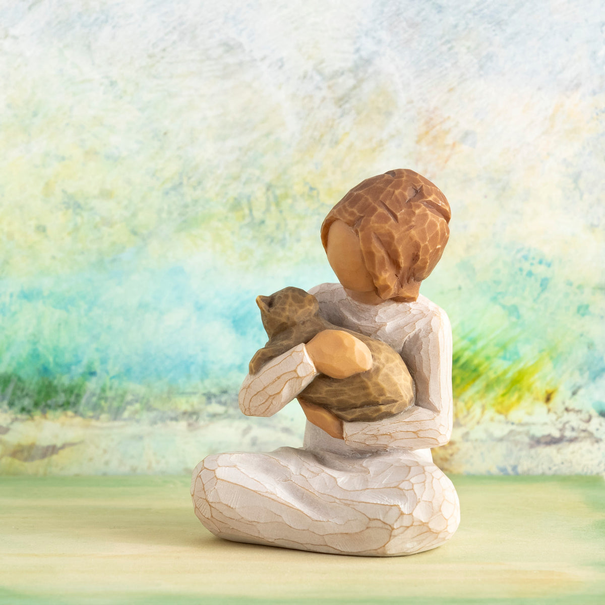 Willow Tree Kindness (girl), 3”h hand-painted resin figure of seated girl in cream dress holding gray cat, in front of light green painting