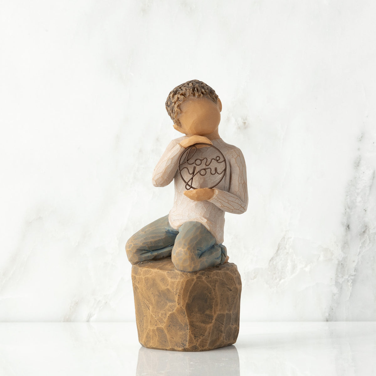 Front view: Figure of lighter-skin child, kneeling on rock, holding wire circle with ‘love you’ written in wire