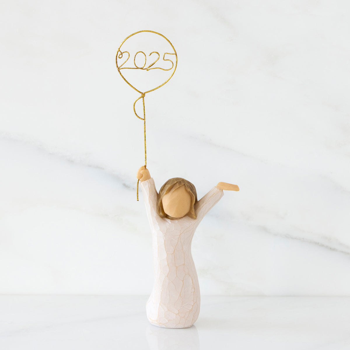 Front view: standing figure in cream dress, arms raised, holding gold wire balloon with 2025 written in gold wire inside