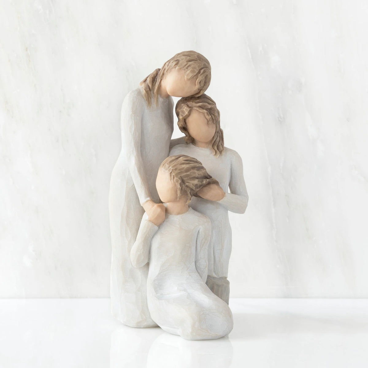 Front view, figurine of three females in cream dresses: one standing with arm around kneeling female, and holding hand of seated female
