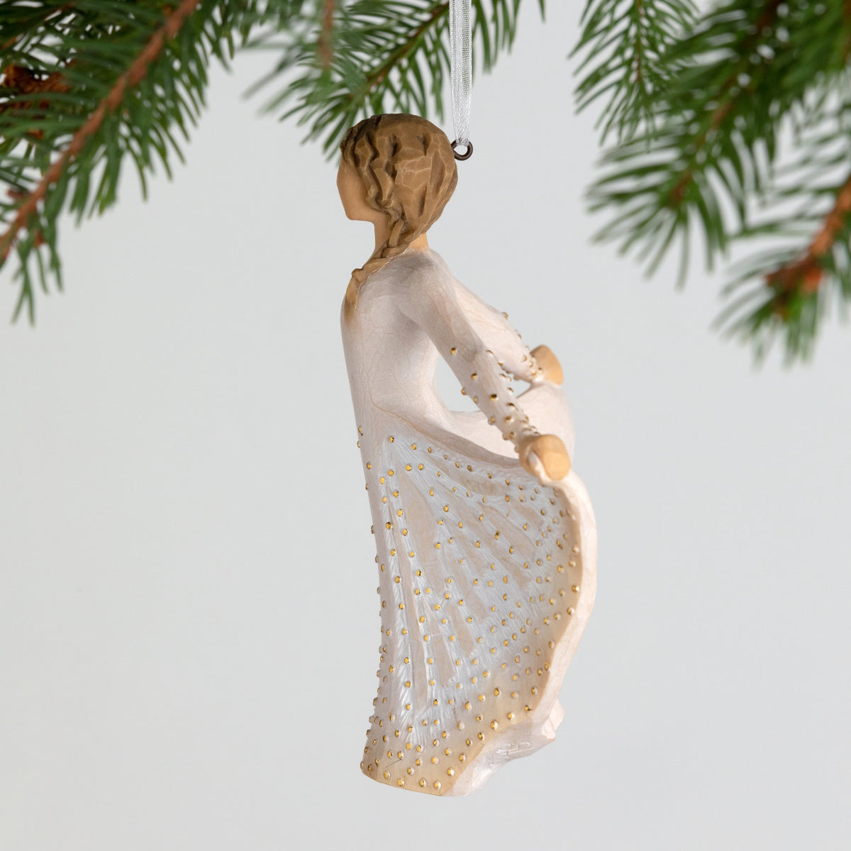 Side view, figure in cream dress, holds skirt with both hands, carved like monarch, dotted with gold. Hook, loop on ornament's head