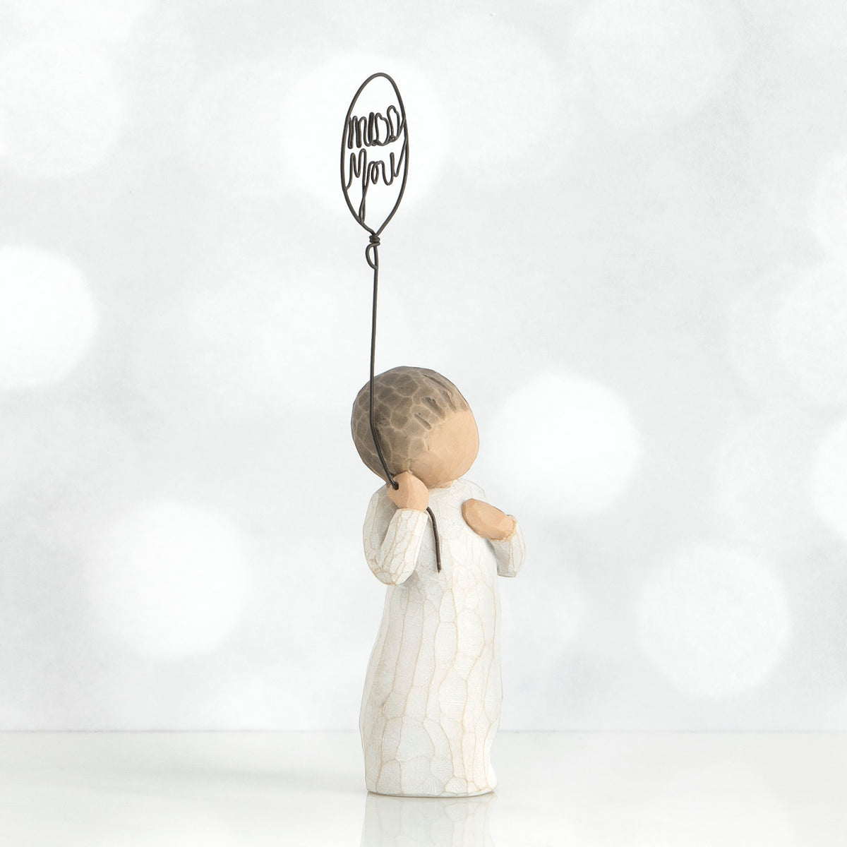 Small boy figurine facing the side in white holding up black wire balloon