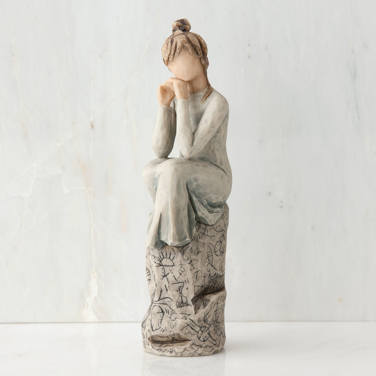 Brunette girl figurine in grey dress sitting on grey rock with her hands to her face