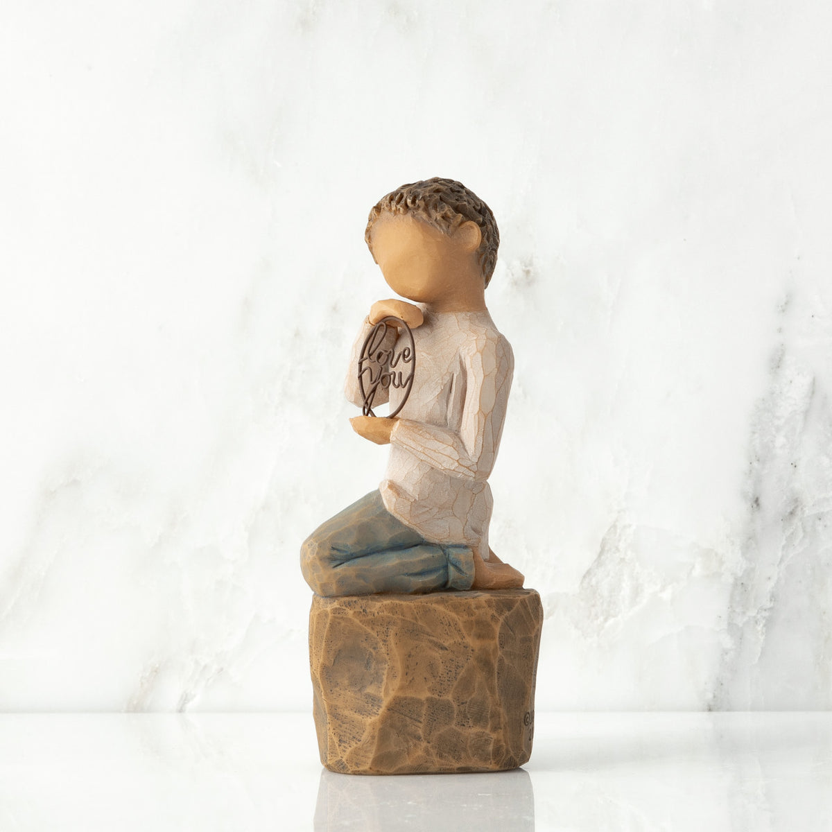 Left view: Figure of lighter-skin child, kneeling on rock, holding wire circle with ‘love you’ written in wire