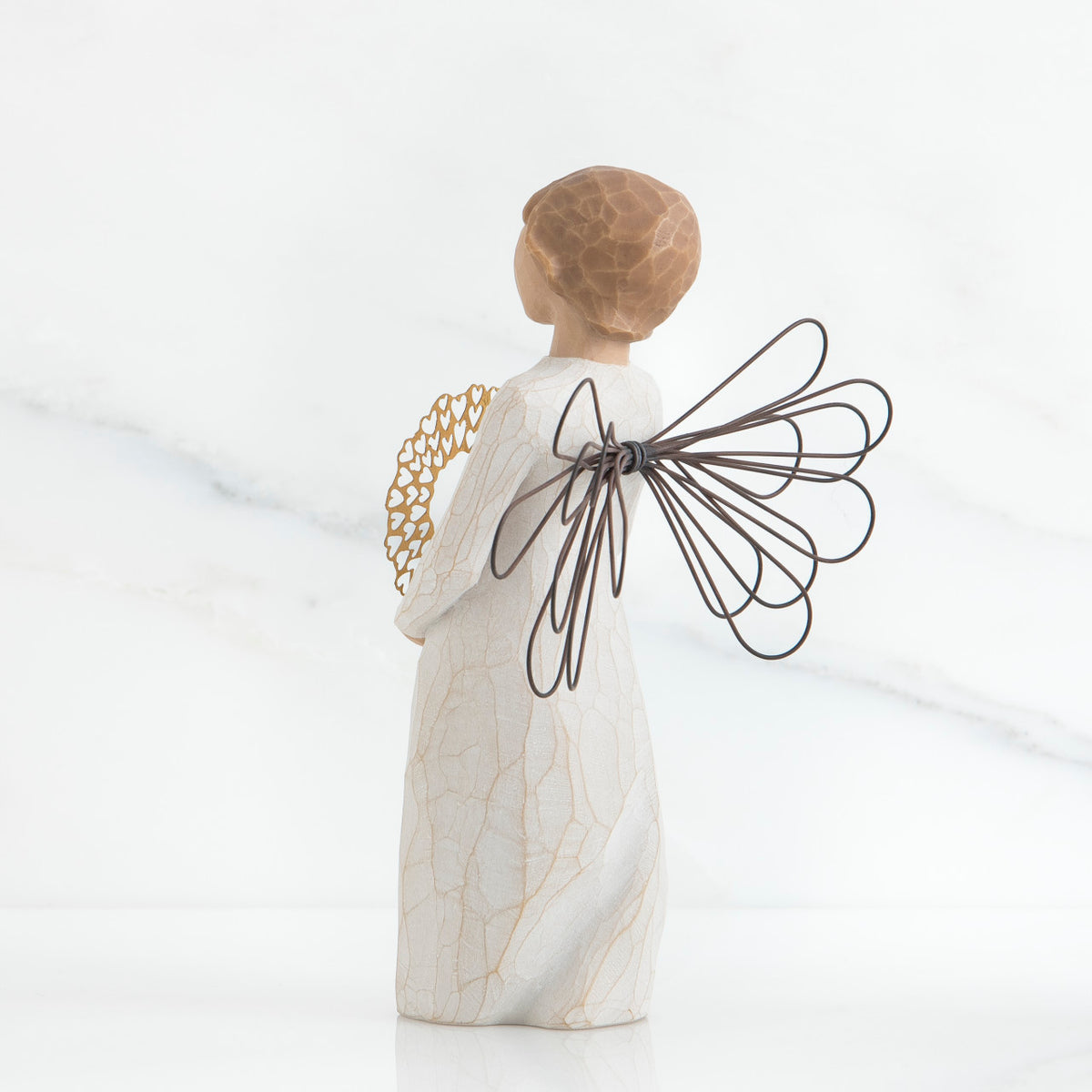 Back view of angel with short, light brown hair holding a metallic wreath of hearts with both hands