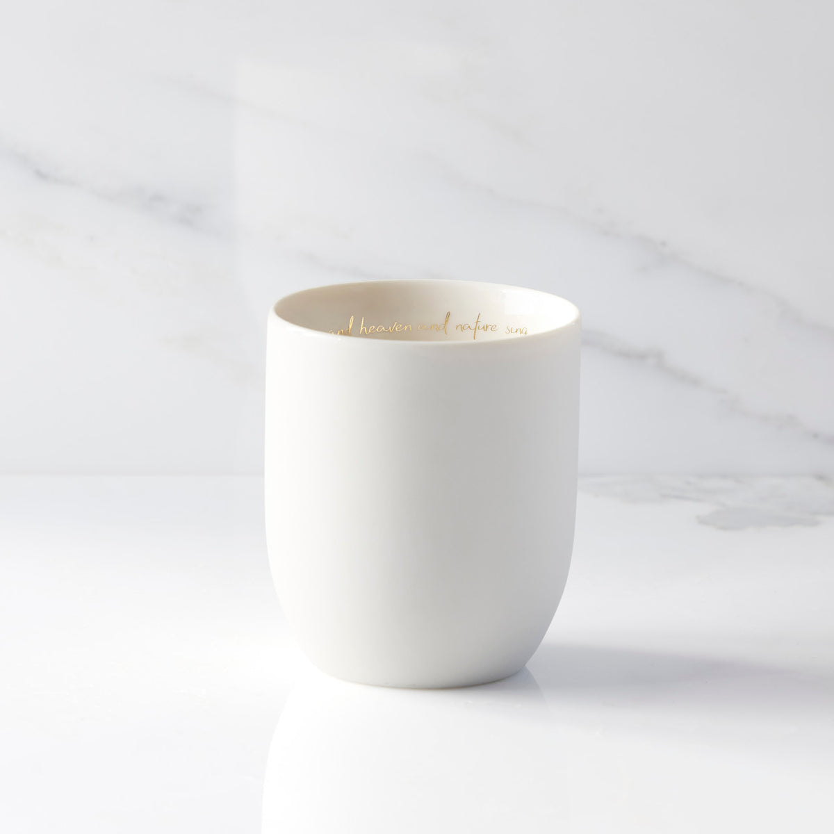 Inside view of unglazed off-white tapered cylinder ceramic candle showing sentiment written in gold along inside rim of vessel