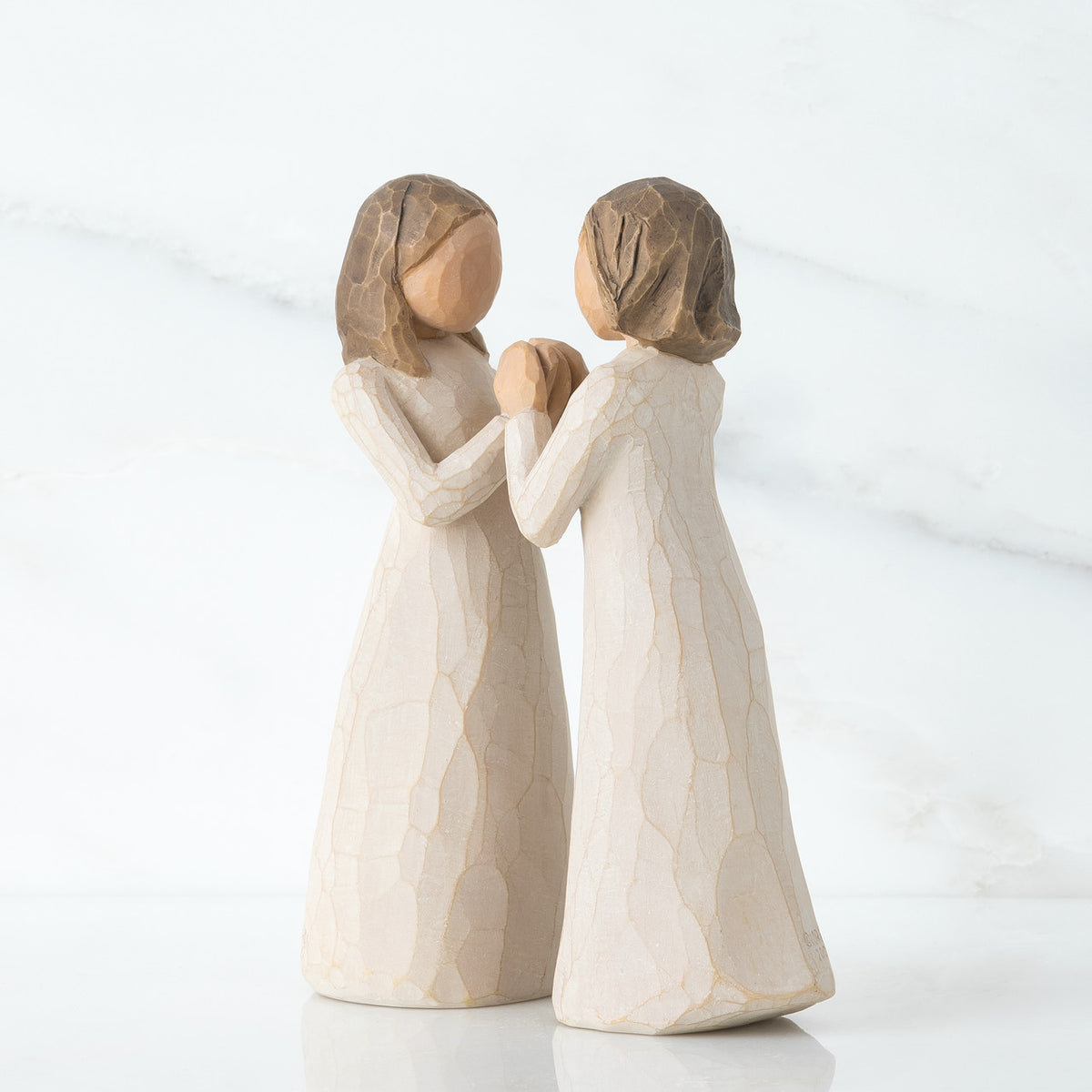Two young girl figurines in white holding hands facing another