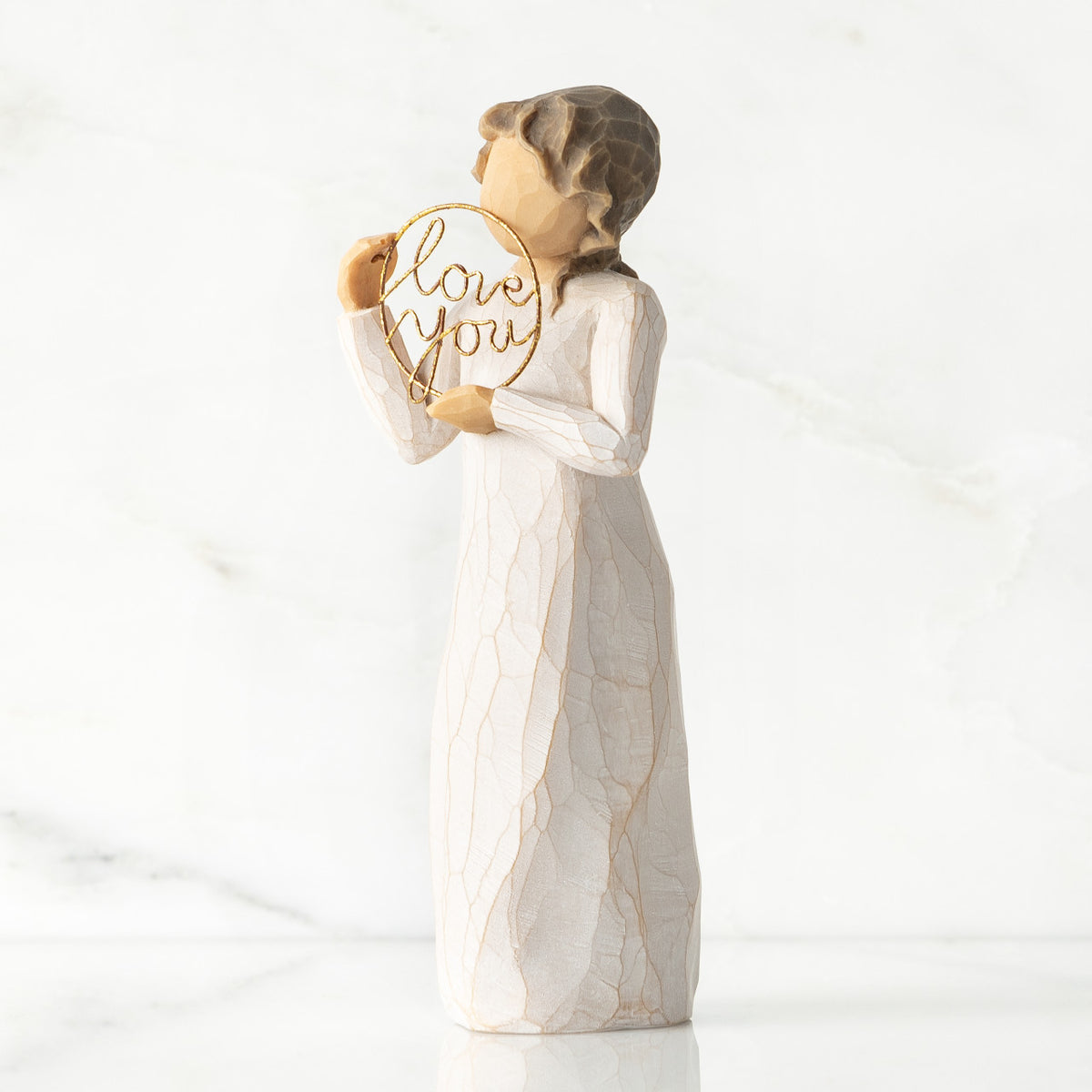 Left-facing view, standing female figure in cream dress, holding gold wire circle in which is written 'love you'