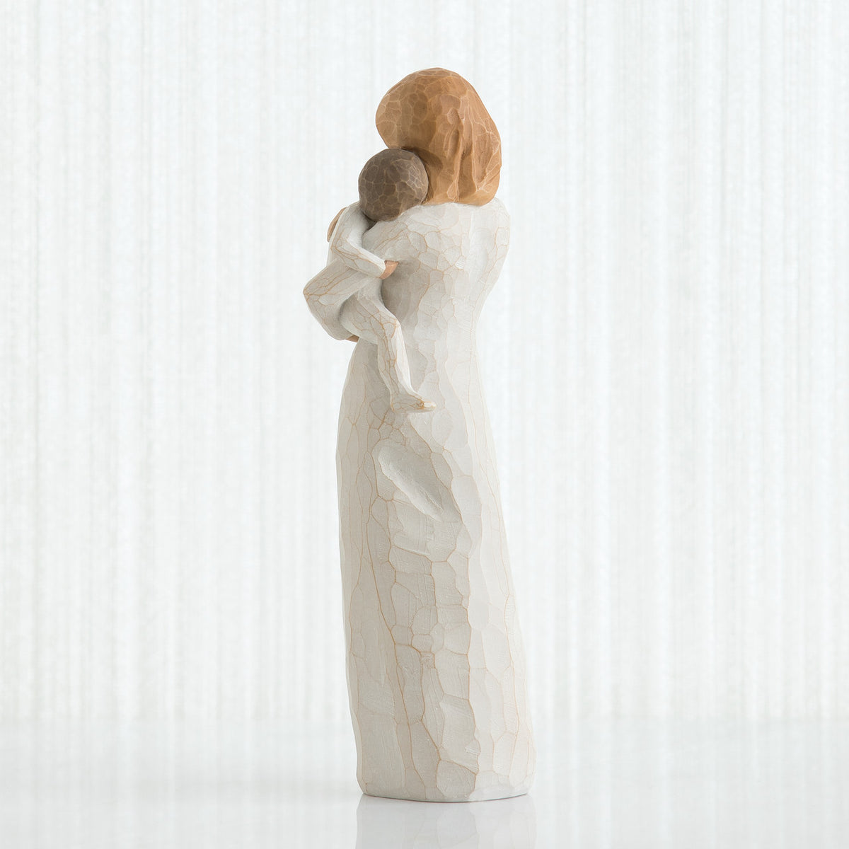 Back view of red haired woman figurine in white dress holding baby