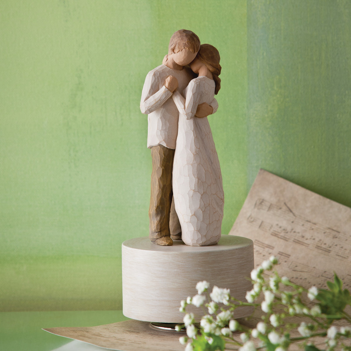 Willow Tree Promise Musical, 8”h hand-painted resin figure of standing couple embracing or dancing, in neutral clothing, atop round, cream base containing musical element, in front of green painting