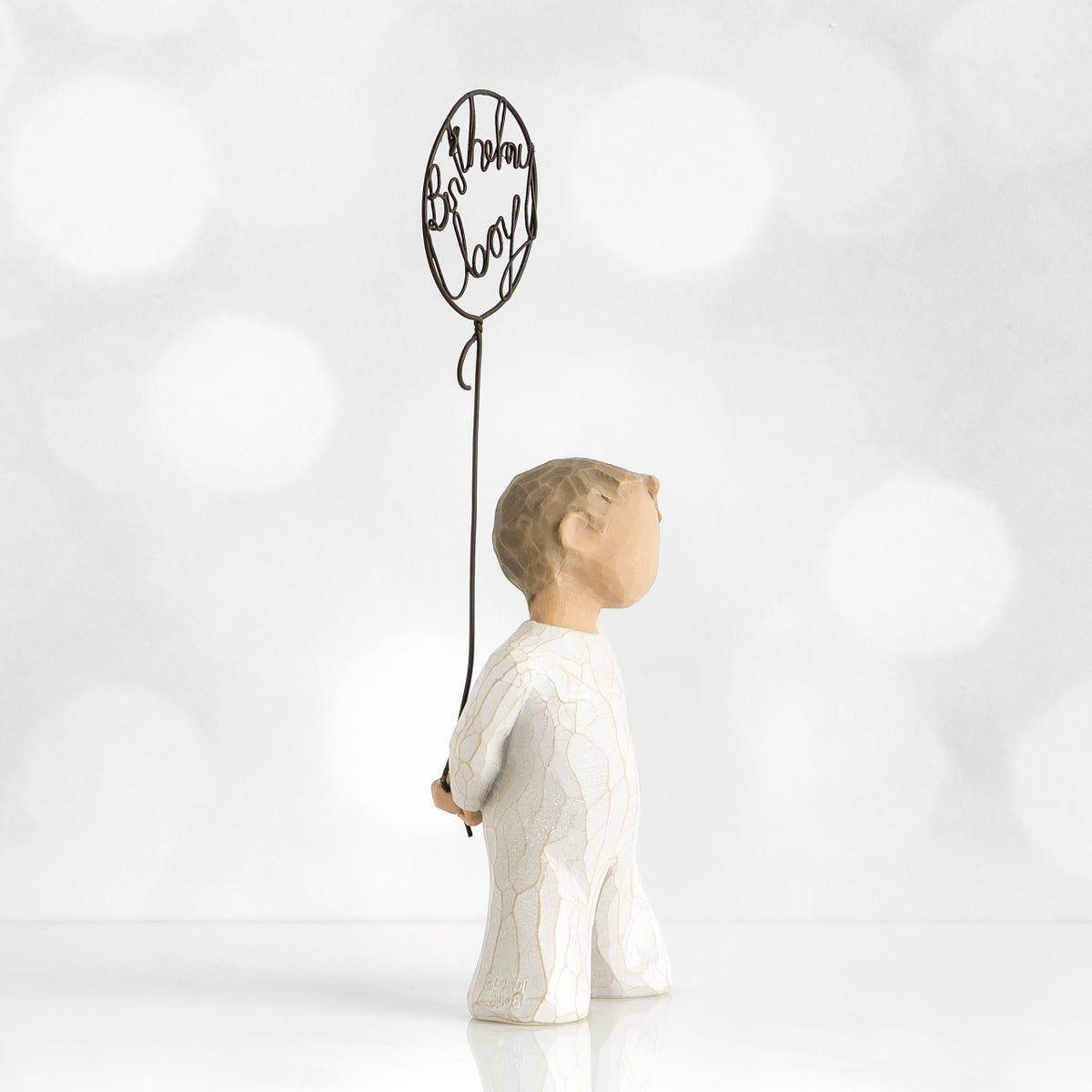 Left side view of little boy with light brown hair holding a wire balloon behind his back. Text on balloon is wire