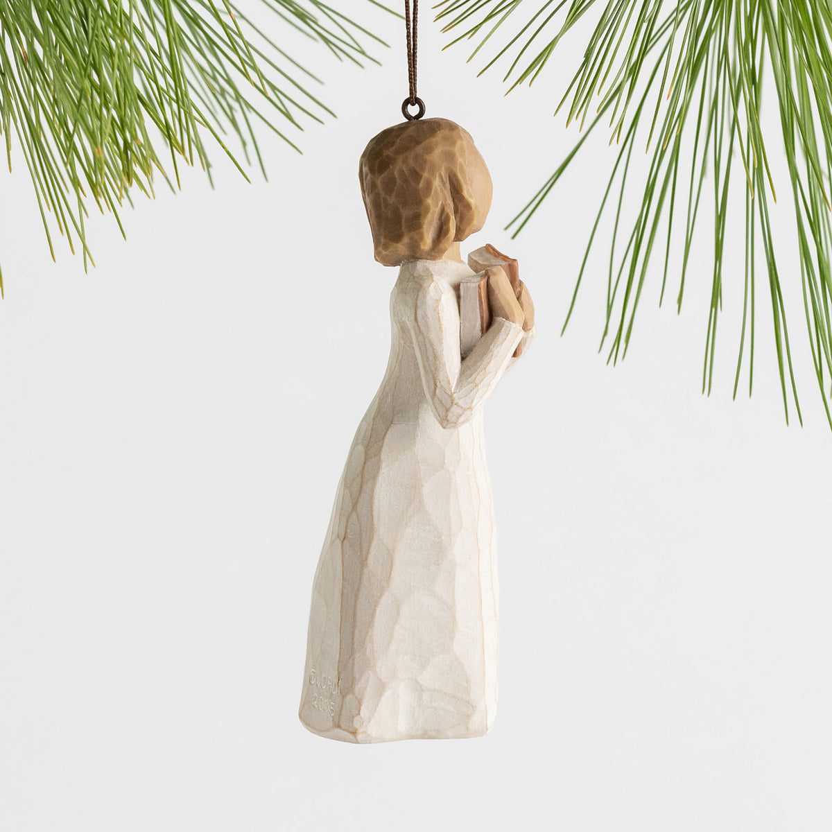 Side view female figure in cream dress, holding open book to her chest, ornament hook and loop attached to head