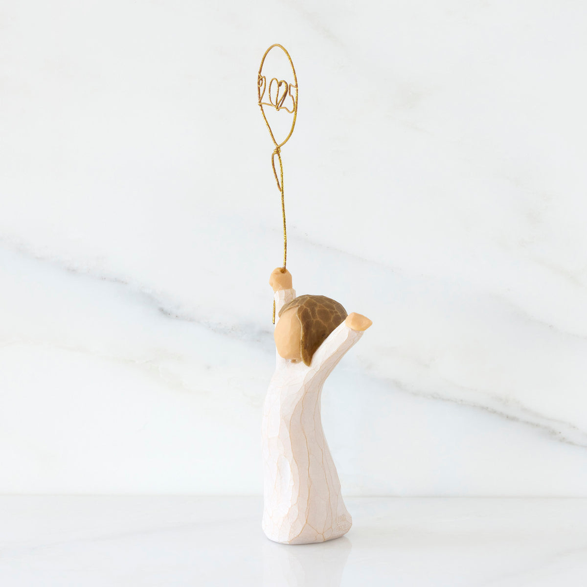 Facing left: standing figure in cream dress, arms raised, holding gold wire balloon with 2025 written in gold wire inside