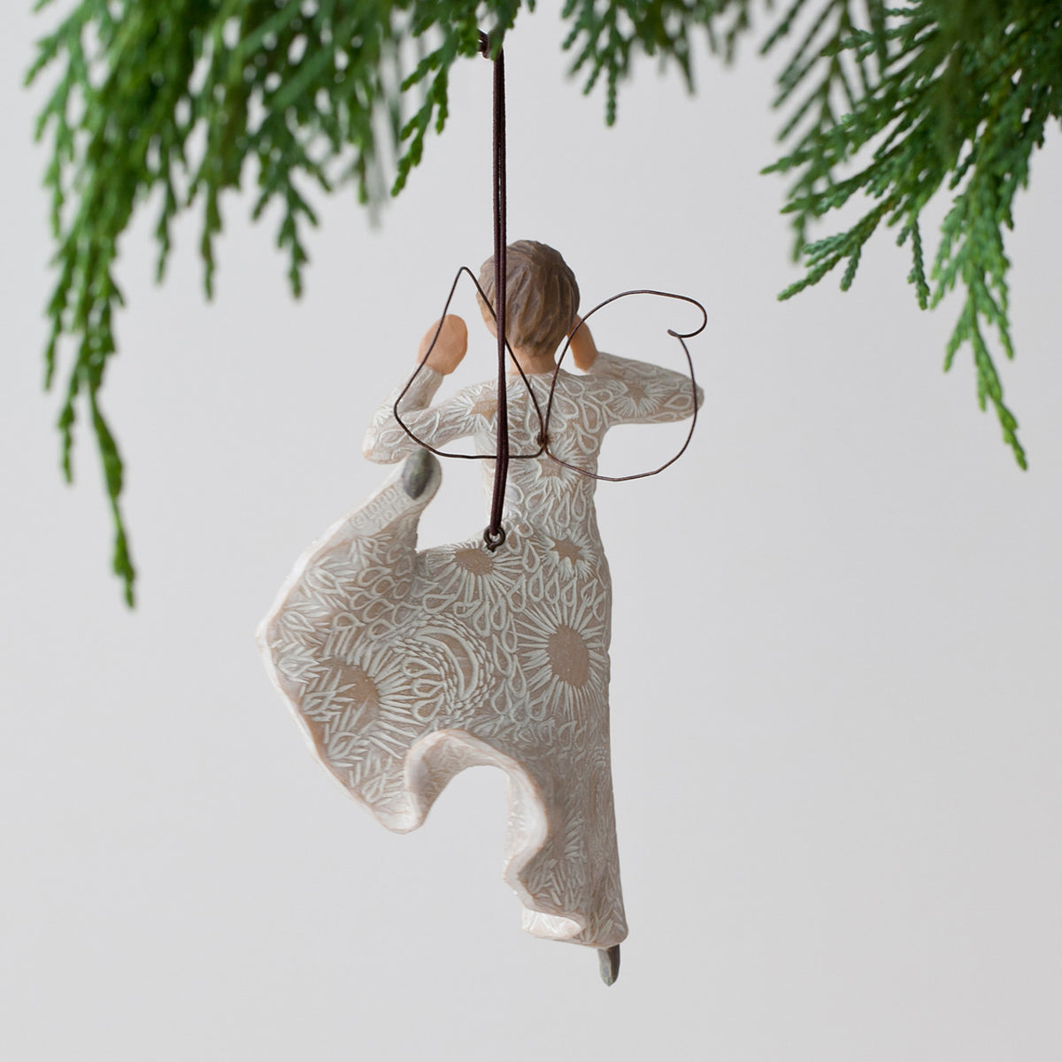 Back view of woman angel figurine ornament in white dress hanging from green tree