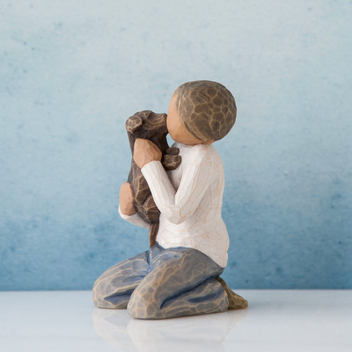 Side view of boy figurine in white shirt and jeans sitting holding brown dog - blue background