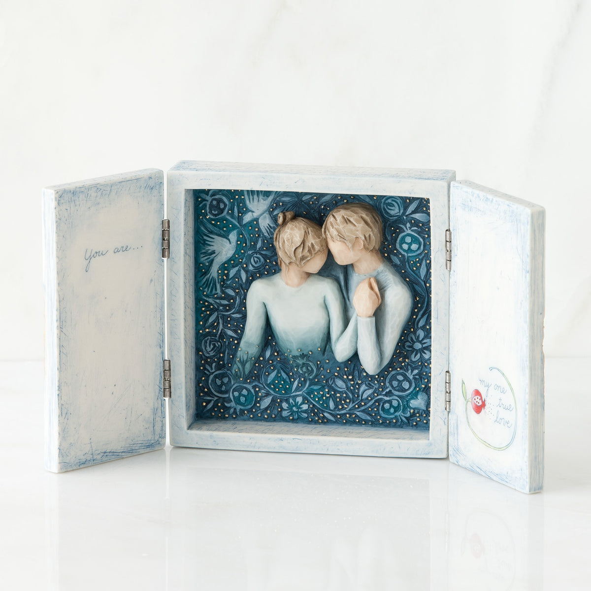 Open white/blue box with image of blue background and man and woman figurine in blue holding hands centered