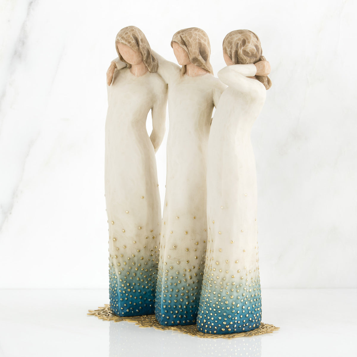 Three brown haired woman figurines with white dresses and blue bottoms with arms on each other