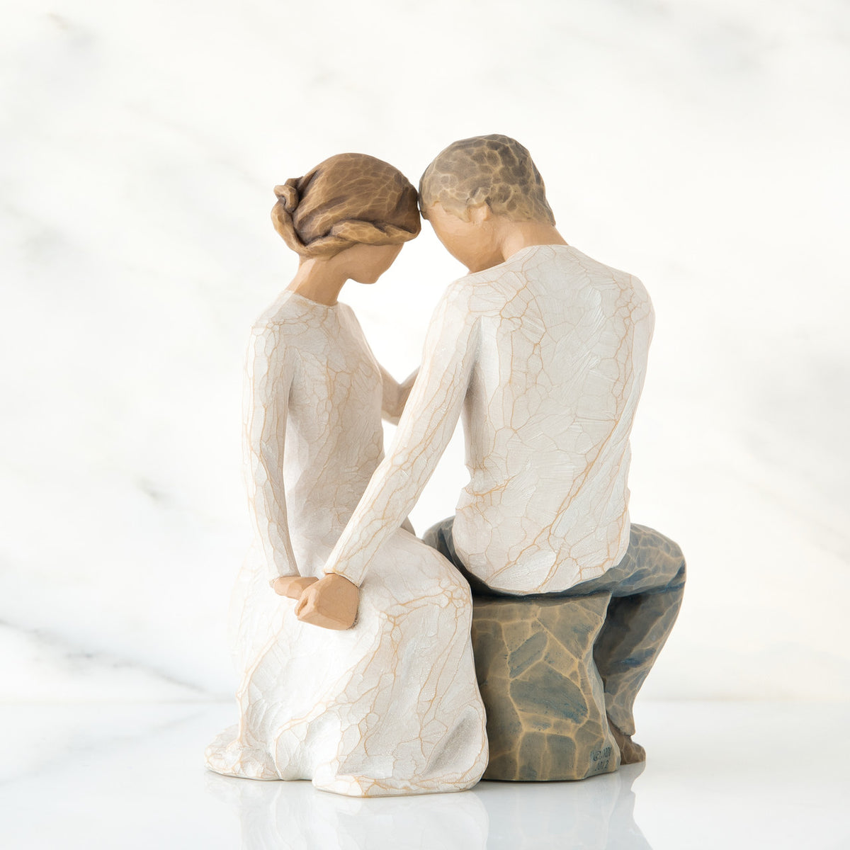 Man and woman figurine in white sitting on rock holding hands facing one another